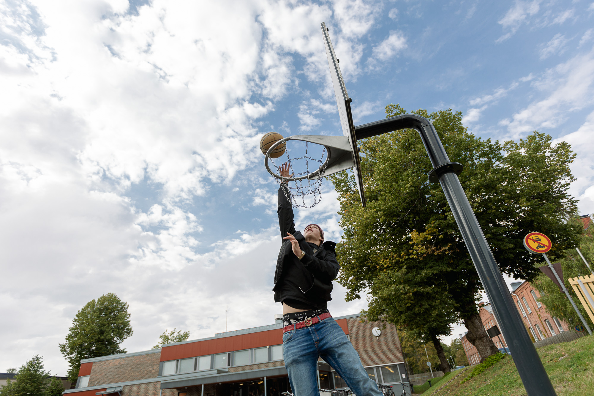 Opiskelija heittää pallon koriin lukion pihalla.